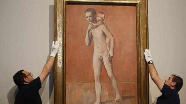Dos operarios cuelgan uno de los Picassos expuestos en El Prado.