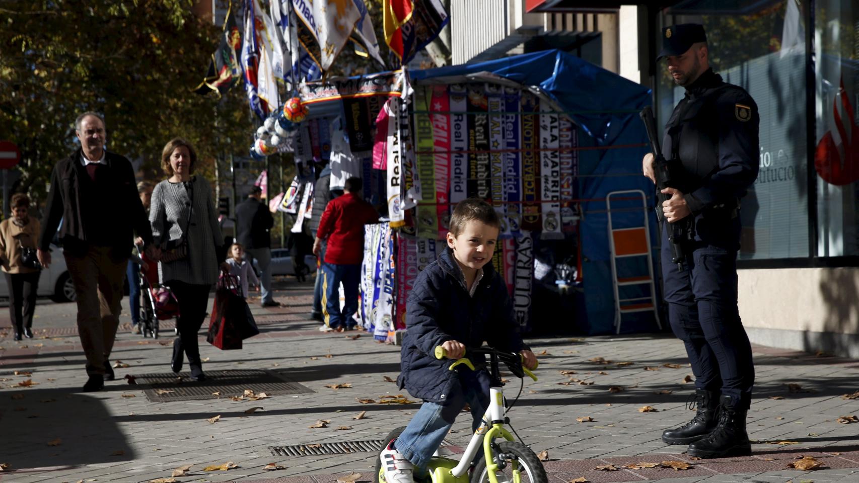 Un niño circula con su bicicleta cerca del estadio bajo la atenta mirada de un policía.