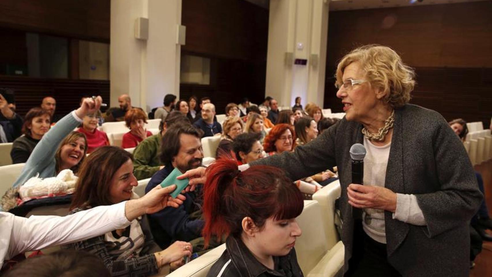 Manuela Carmena reparte ceniceros durante una conferencia sobre educación.