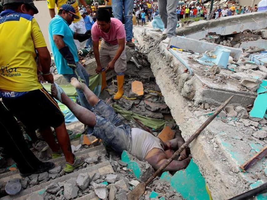 nas personas rescatan un cuerpo entre los escombros en la localidad de Pedernales.