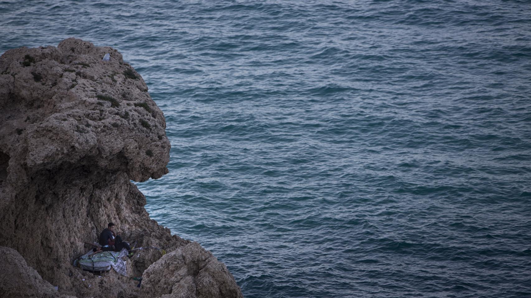 Dos menores sobre un colchón tirado cerca del espigón del puerto de Melilla.