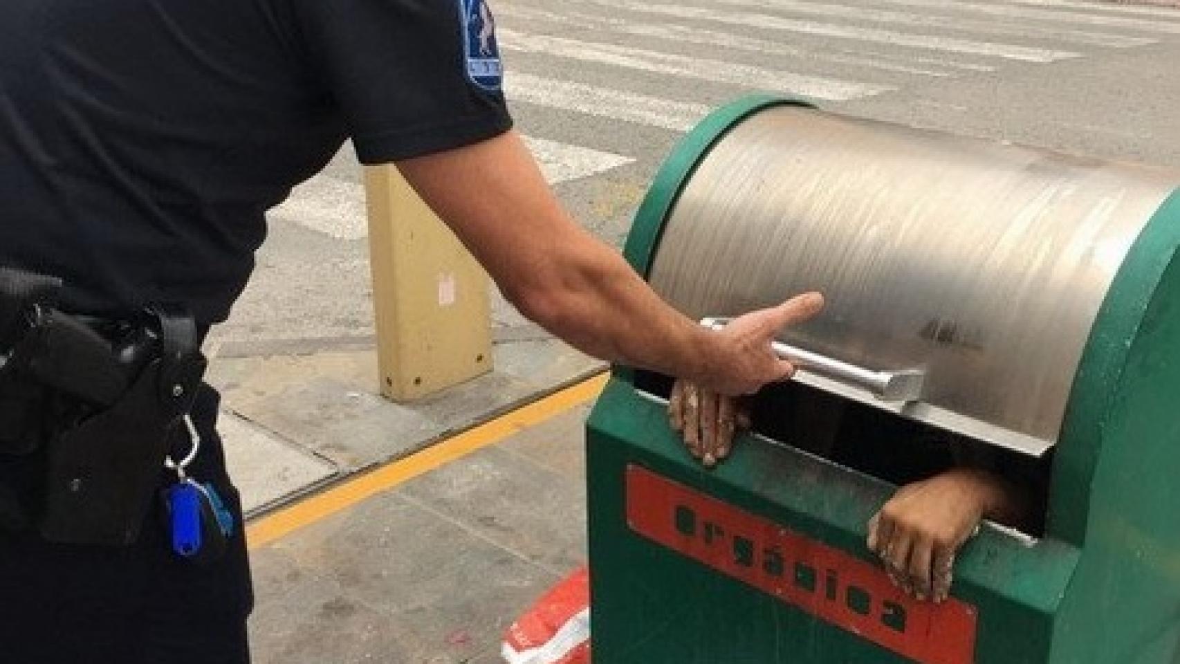 Un agente de la Policía Local intenta abrir la trampilla del contenedor.