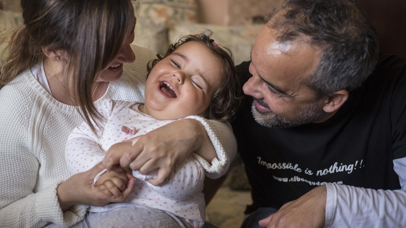 Alba, sonriente entre sus padres, Belén y Sergio.