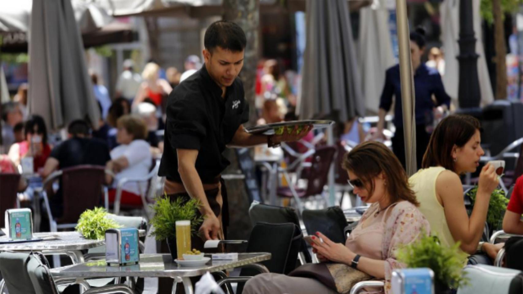 Un joven camarero sirve una consumición en una terraza.