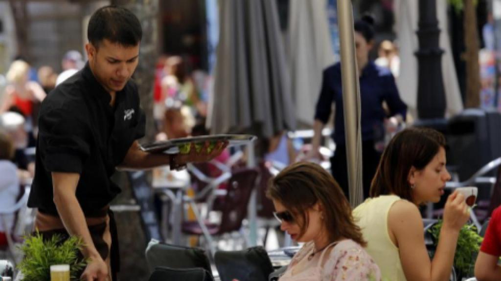 Un joven camarero sirve una consumición en una terraza.