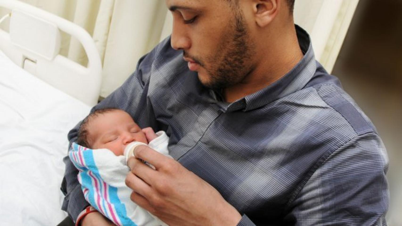 Un hombre da el biberón a un bebé que tiene cogido.