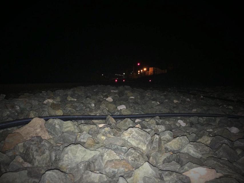 Nada más salir del andén, las piedras junto a las vías son del tamaño de puños. Al fondo, un polígono industrial iluminado.