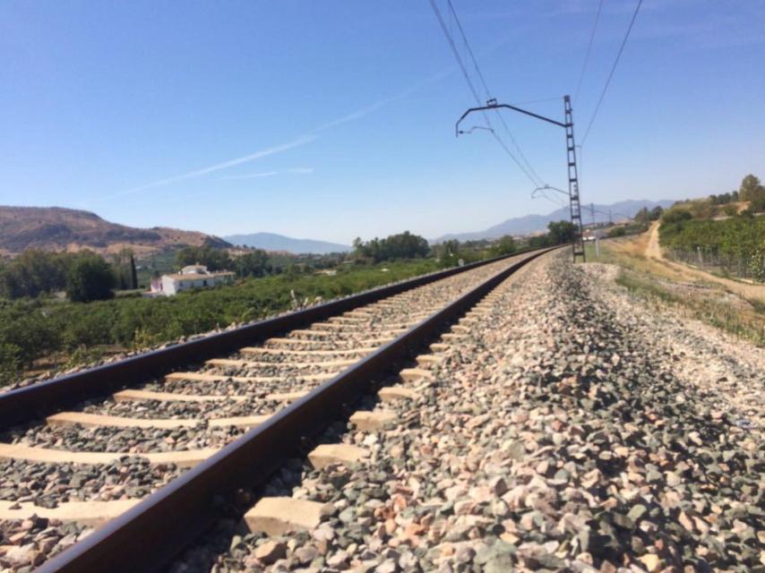 Las vías del tren discurren entre huertas y algunas casas, accesibles a pie desde la ruta ferroviaria.