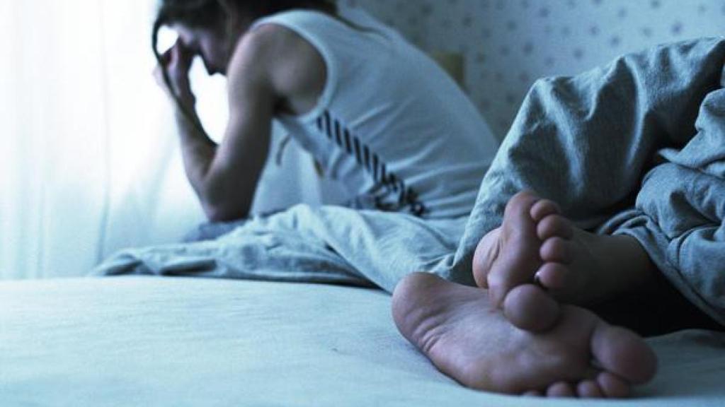Un hombre duerme mientras su pareja está sentada en el borde de la cama.