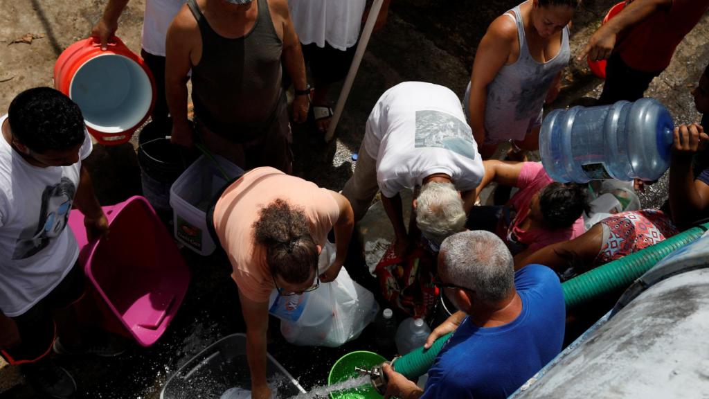 Varias personas esperan para coger agua proporcionada por un camión de ayuda