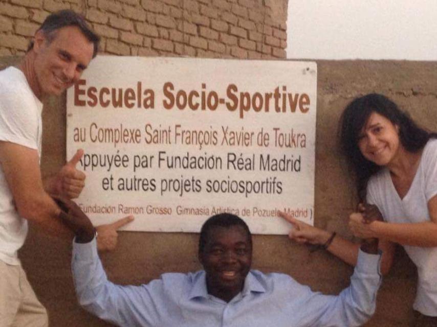 Ramón Grosso, el Padre Camille y Sylvia García posan junto al cartel del colegio.