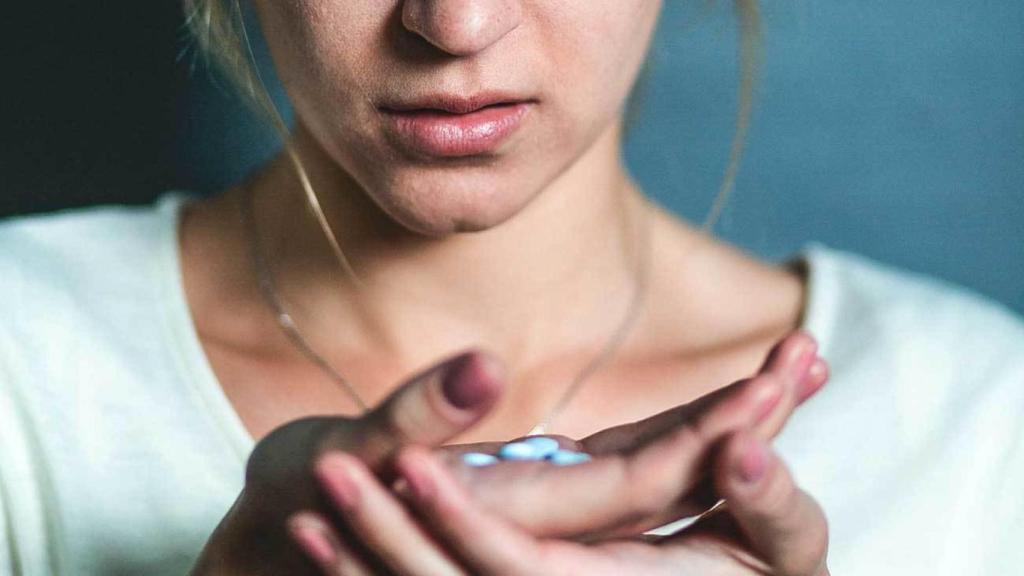 Una mujer tomándose una pastilla.