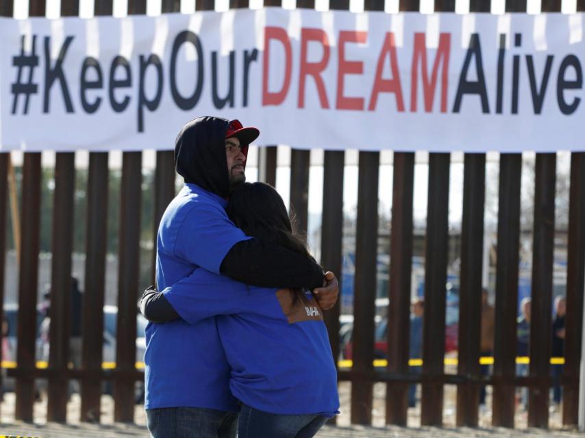 Dos manifestantes contra las políticas de Trump se abrazan frente a la frontera de México