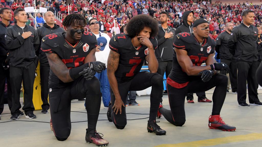 Colin Kaepernick (centro), arrodillado con dos compañeros de equipo.