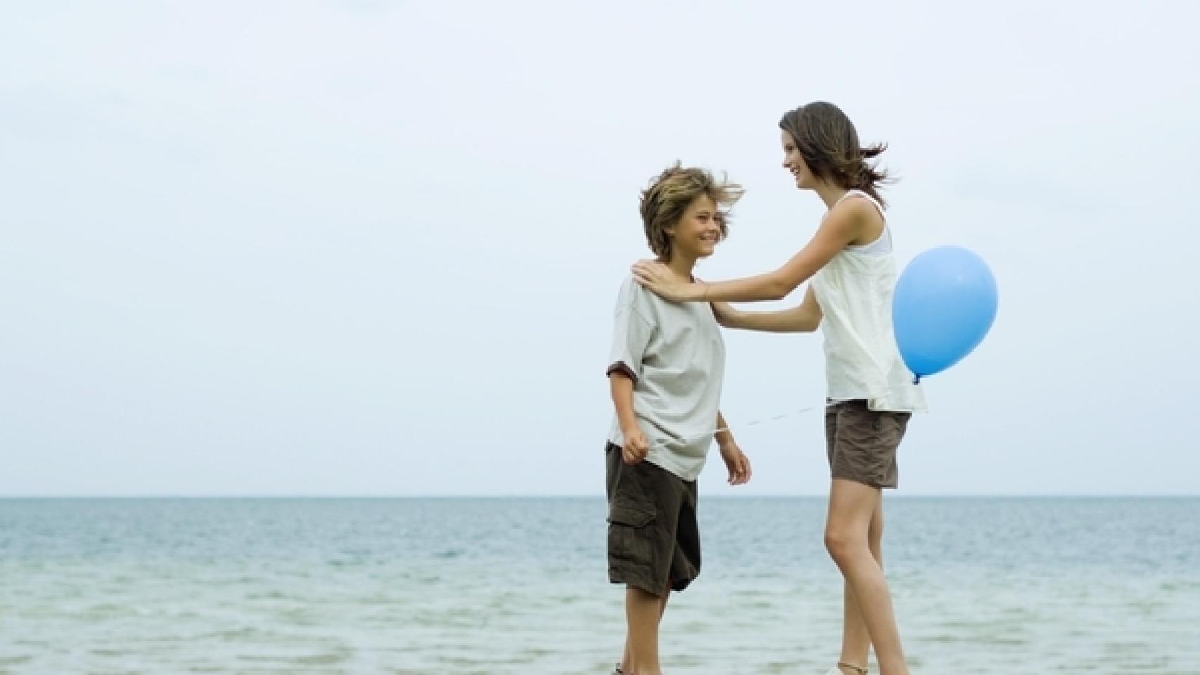 Dos hermanos juegan con un globo de plástico frente al mar.