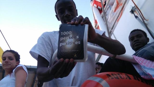 Foto del joven con el libro que ha leído al resto de migrantes del Aquarius.