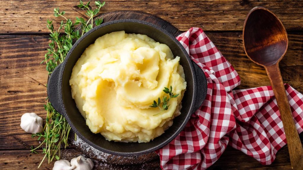 Mashed potatoes, boiled puree in cast iron pot on dark wooden rustic background, top view