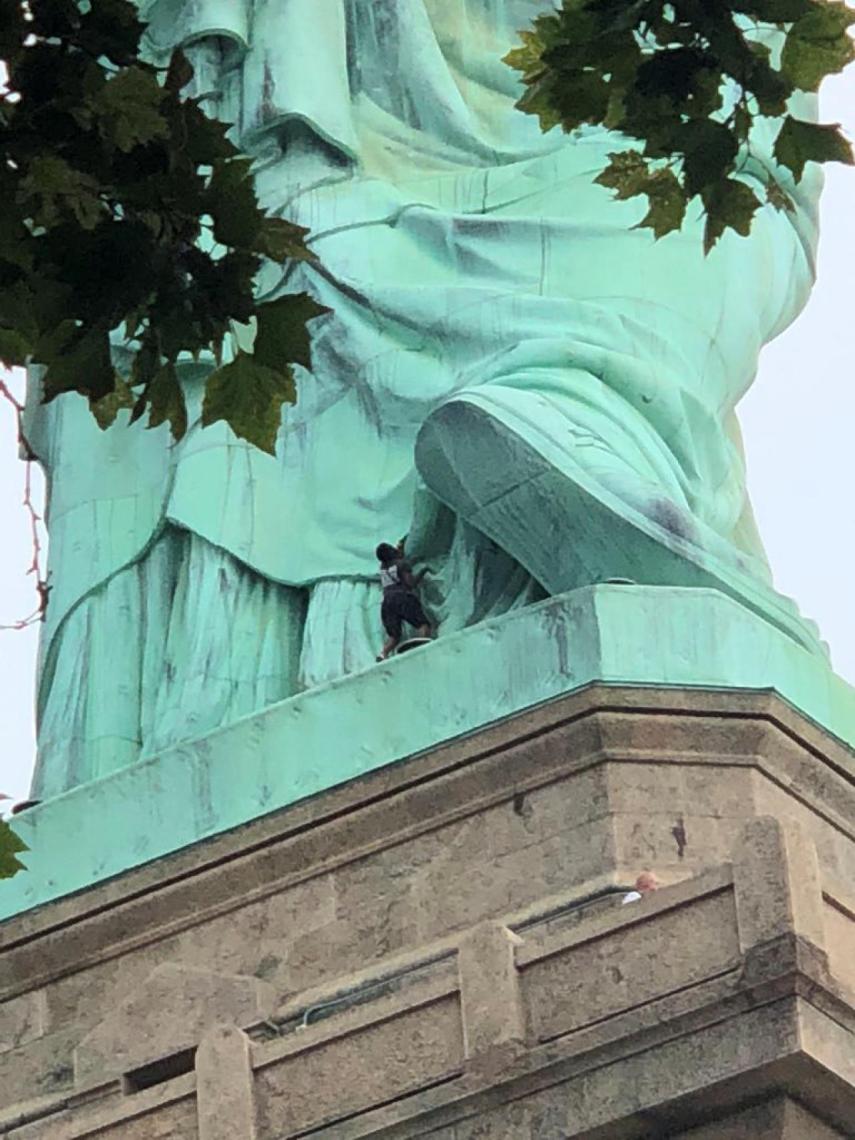 Momento en que la mujer trepa hasta el pedestal de la estatua de la Libertad.