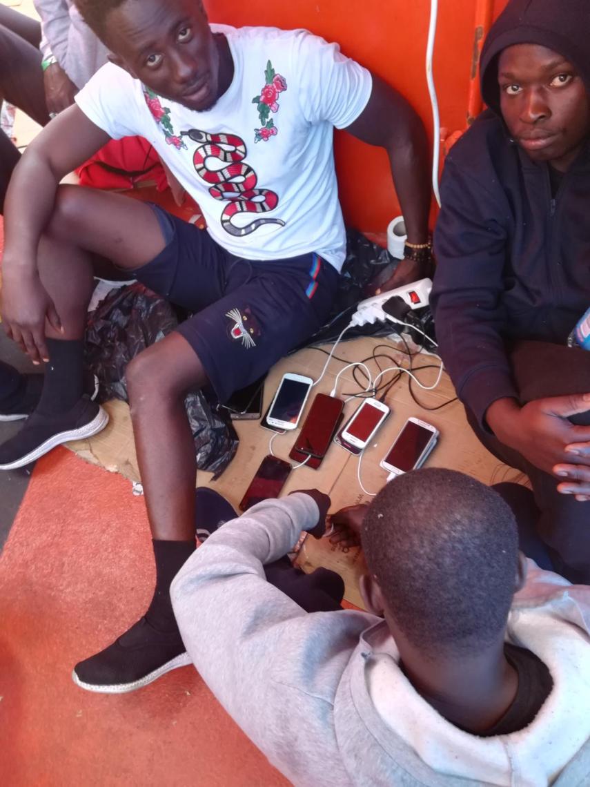 Varios inmigrantes cargan las baterías de sus teléfonos móviles en el buque María Zambrano, donde han permanecido cuatro días.