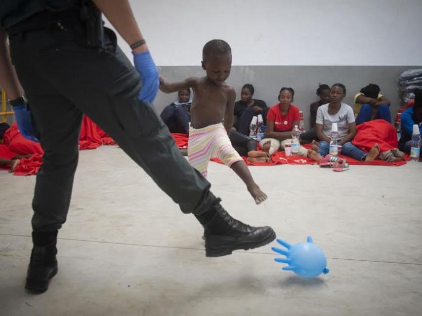 Un agente de la Guardia Civil juguetea con un niño de origen subsahariano con un globo hinchado en el puerto de Barbate (Cádiz). La imagen fue tomada durante la última crisis migratoria sufrida por España este verano.