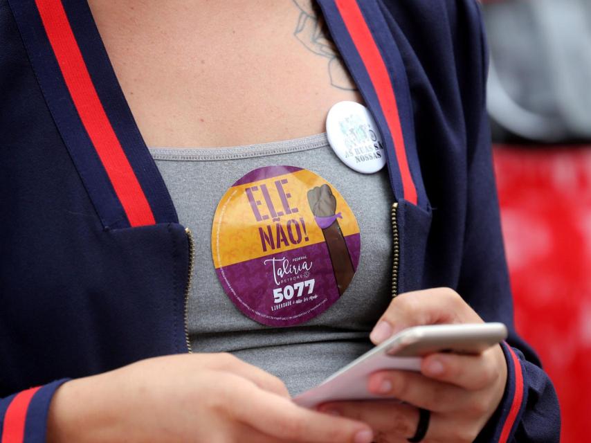 Una chica con una pegatina anti Bolsonaro mira el móvil.