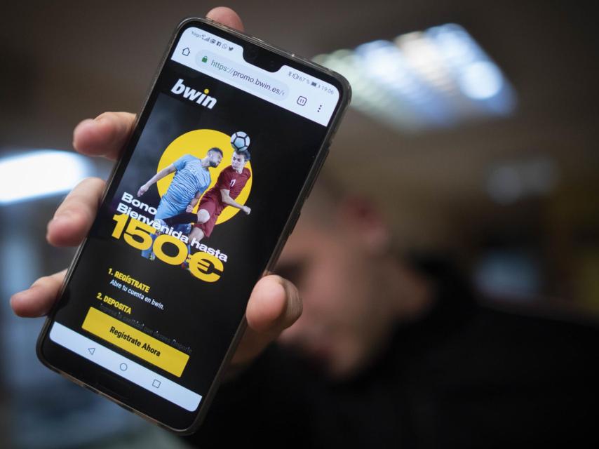 Alejandro, de 21 años, esconde su rostro detrás de un teléfono con publicidad de una casa de apuestas deportivas.