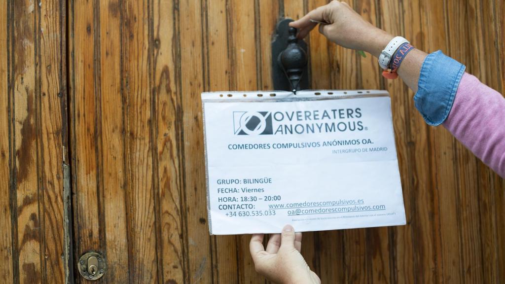 María colocando el cartel de Comedores Compulsivos Anónimos (OA en inglés)  en la puerta de la habitación.