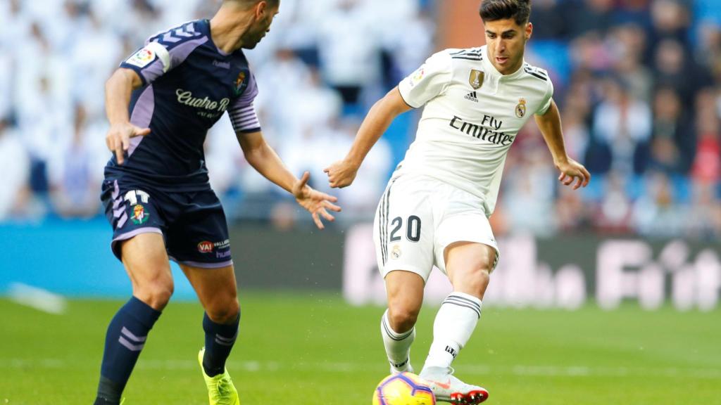 Marco Asensio pasa un balón con un jugador del Valladolid frente a él