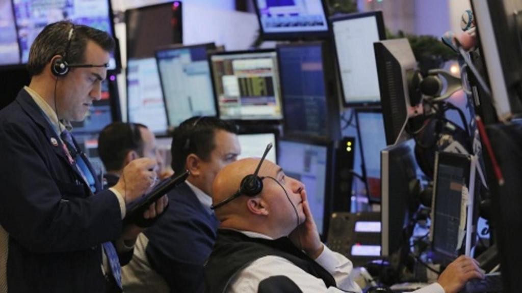 Varios brókeres consultan pantallas en un parqué de bolsa.