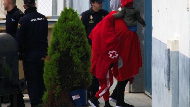 Varios migrantes, con un menor en brazos, entran custodiados por la Policía en el centro temporal del muelle de Algeciras.