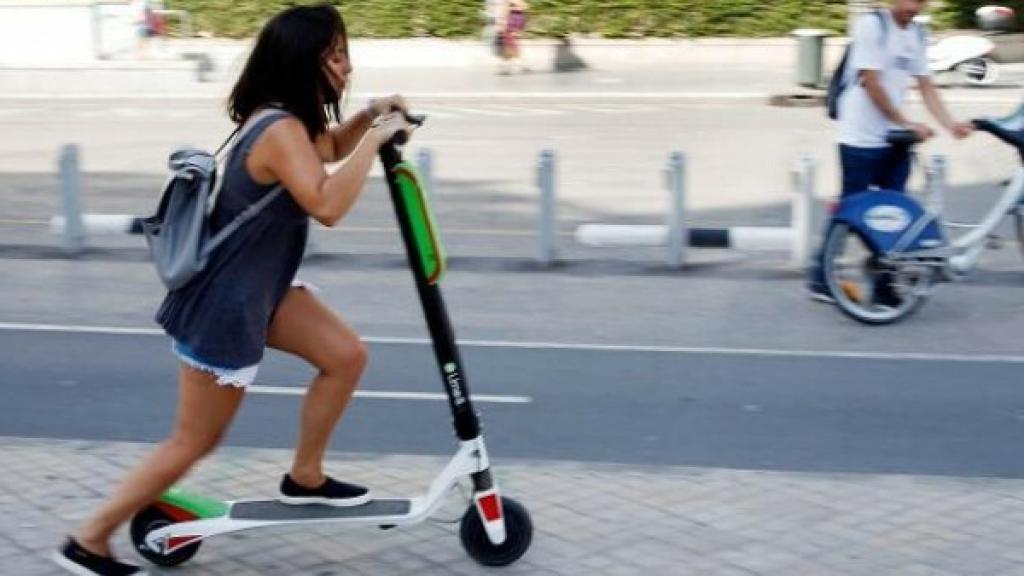 Joven circulando con patinete por la acera
