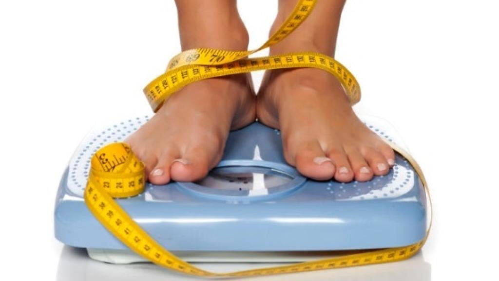 Una joven subida en una báscula con una cinta métrica.