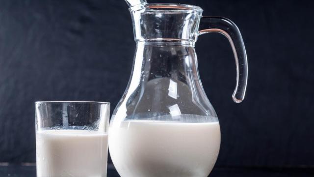 Una jarra llena de leche junto a un vaso.