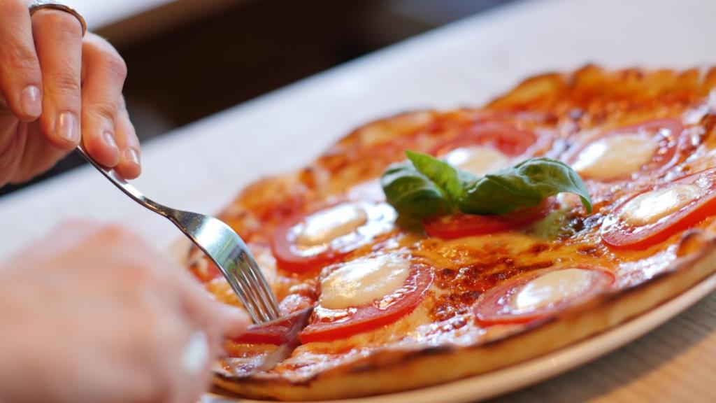 Una persona intentando coger un trozo de pizza con un tenedor.