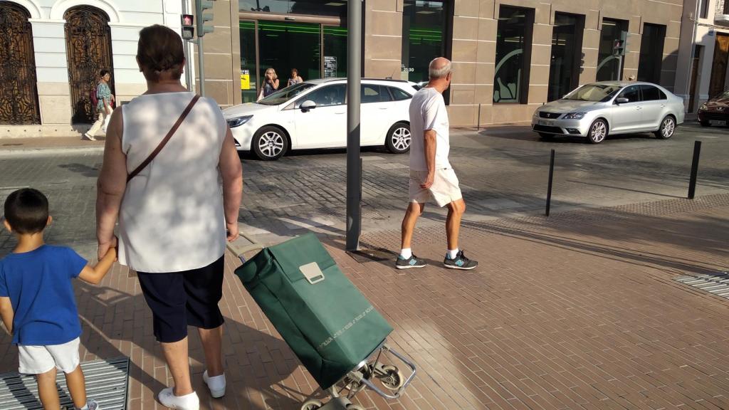 Una abuela se dispone a cruzar, con un carrito de la compra, junto a su nieto, para entrar en el Mercadona de Tavernes Blanques