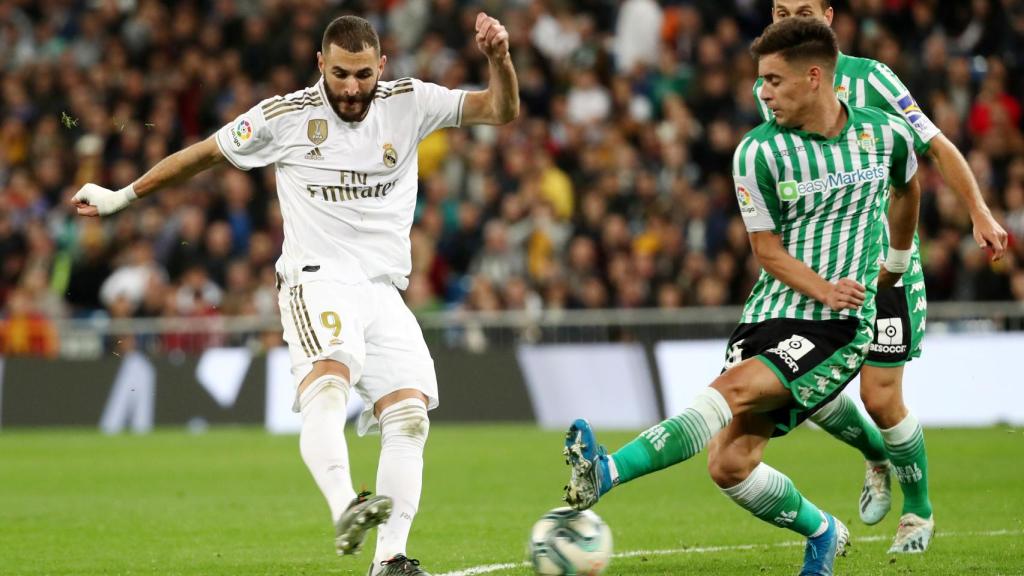 Benzema disparando a la portería del Betis presionado por un rival