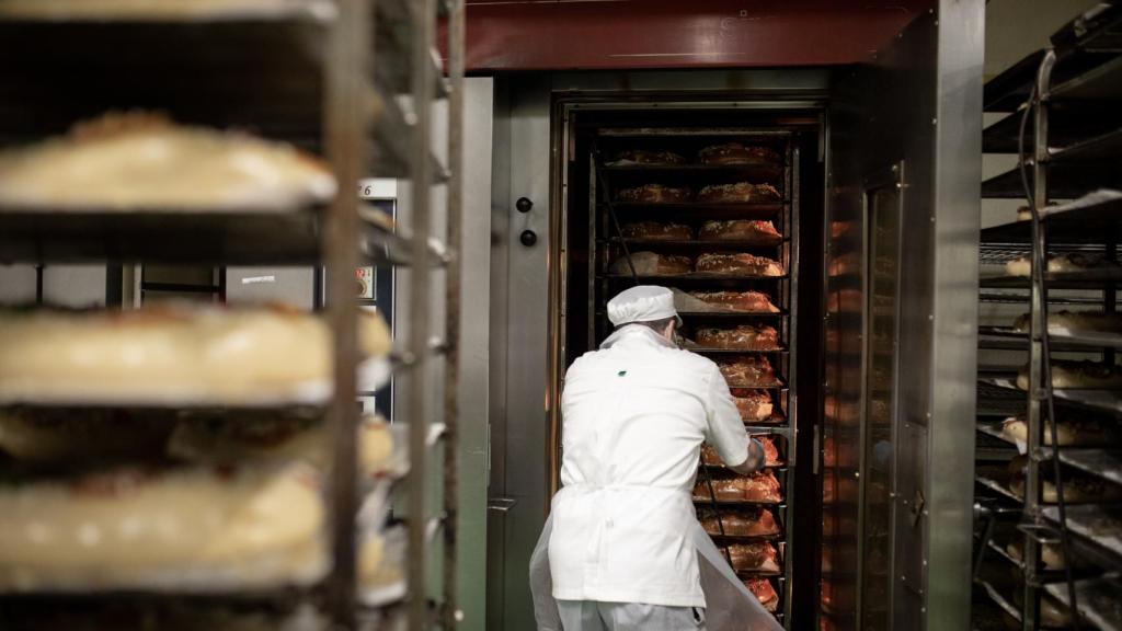 Un pastelero saca del horno un carro de roscones de Reyes.