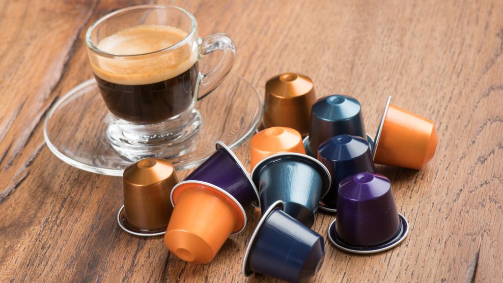 Unas cápsulas rodeando a un café recién hecho.