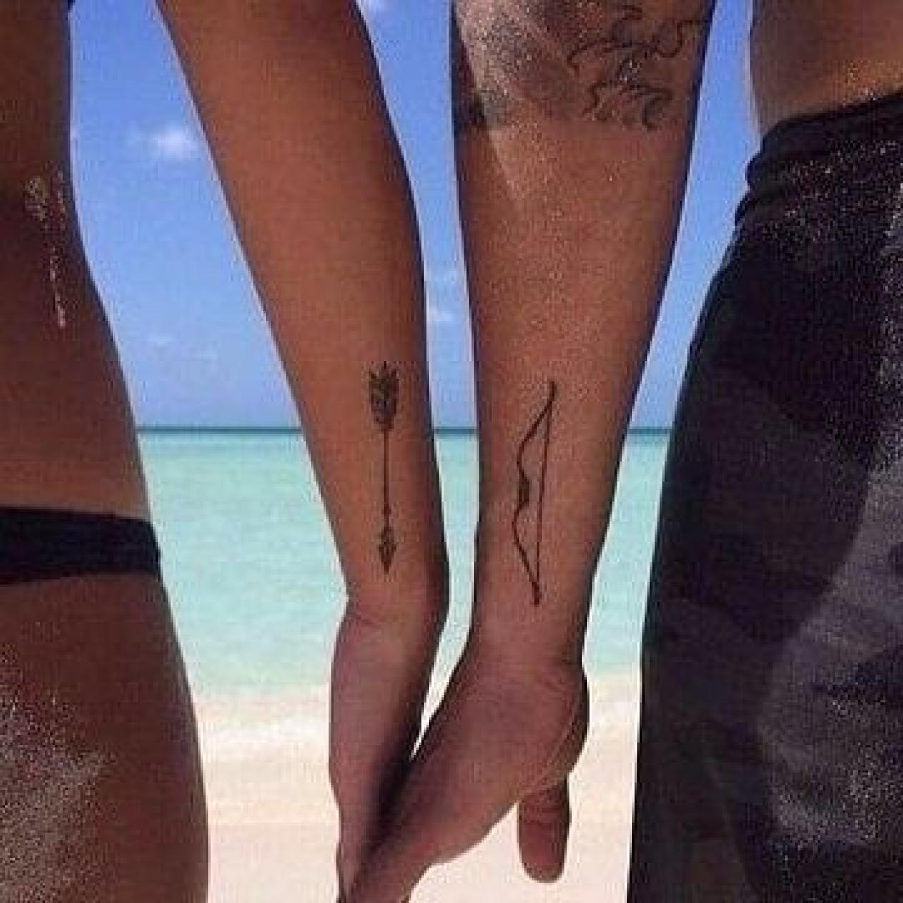 Pareja con tatuajes a juego: ella, una fecha; él, un arco.