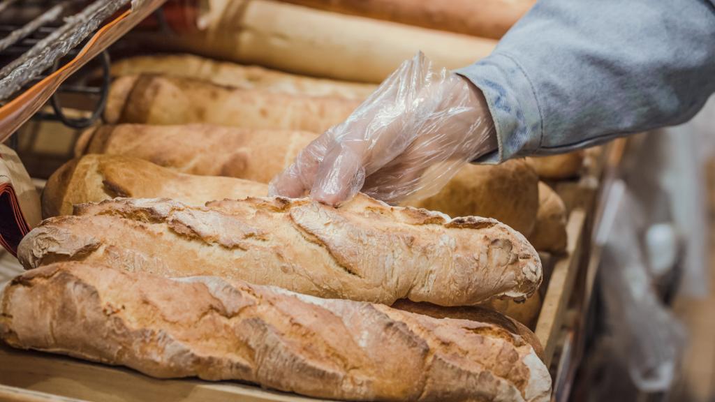 Una persona toma una barra de pan con un guante.
