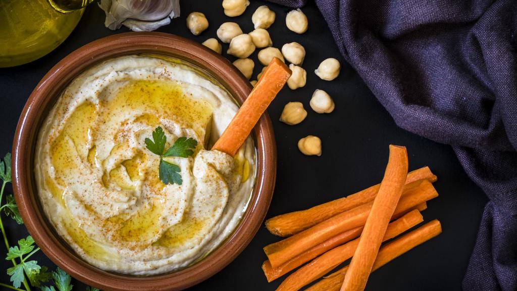 Un plato de barro con hummus y unos palitos de zanahoria.