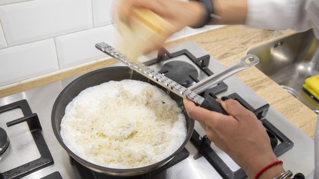 La chef Bárbara, antes de añadir las espinacas trituradas, ralla queso parmigiano en el risotto.