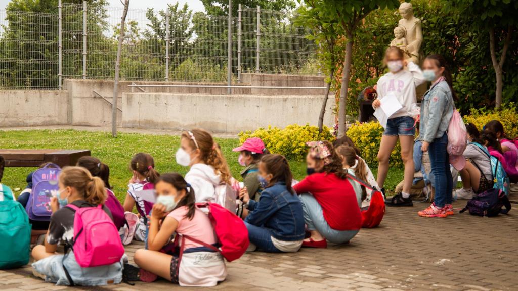 Varias niñas se arremolinan en el recreo de Fuenllana durante una actividad, con la estatua de la Virgen de fondo.