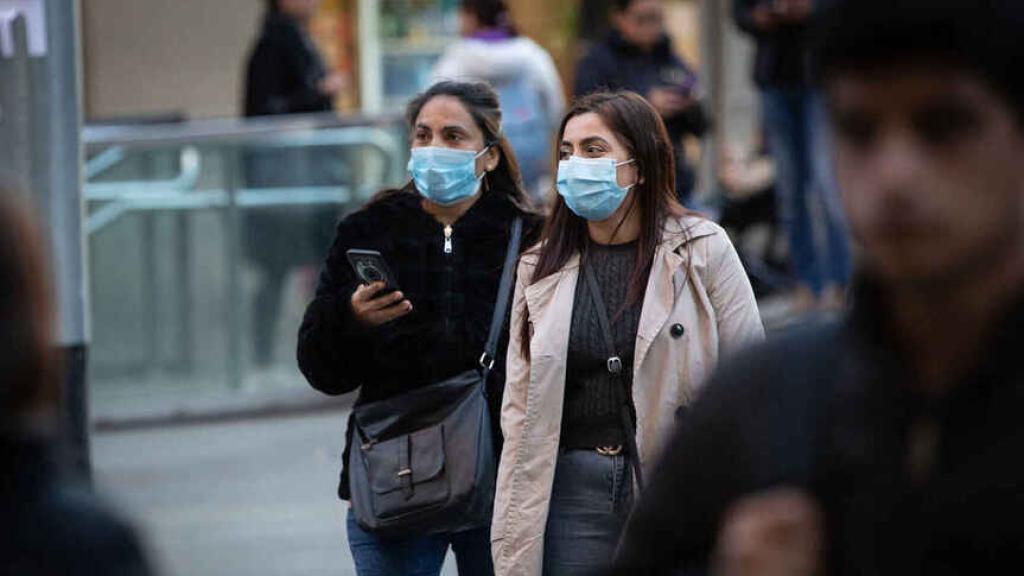 Dos chicas usando mascarilla en la calle.