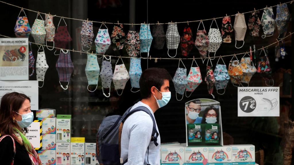 Personas pasean frente a un escaparate donde se muestran mascarillas en Ronda.