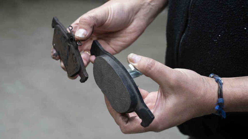 Un mecánico enseña la pastilla de freno desgastada, en su mano derecha, y la nueva, en la izquierda.