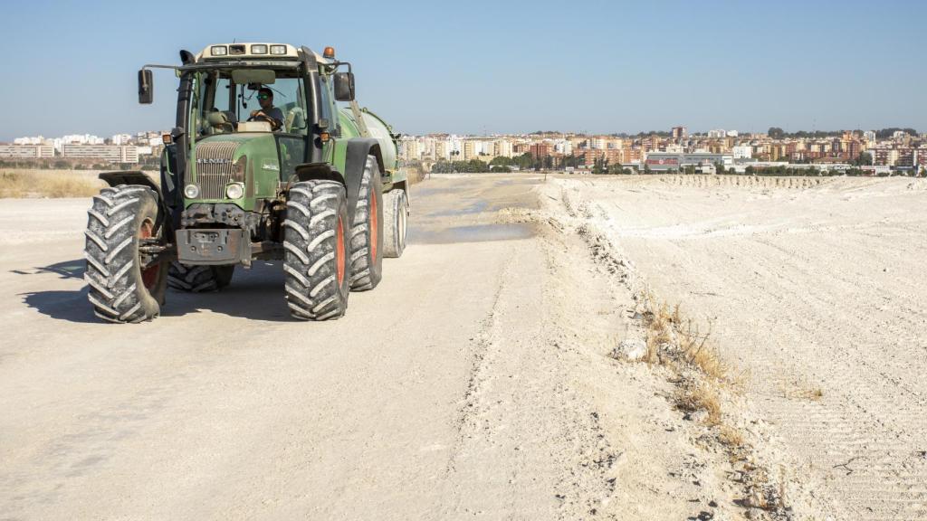 Un operario esparce agua para evitar que el polvo se levante con el paso de los vehículos.