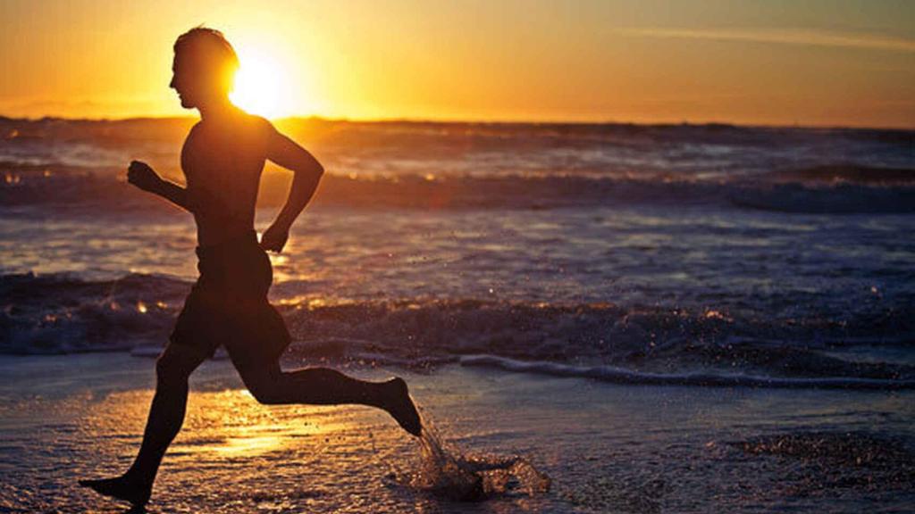 Un hombre corre por la playa en horario de menor incidencia solar.