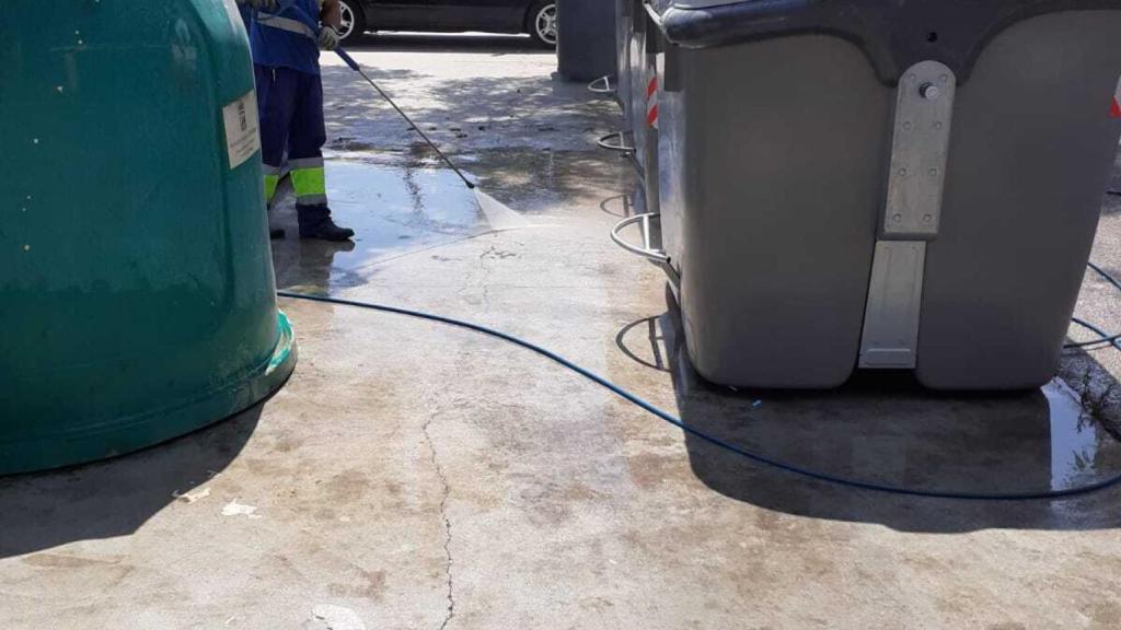 Un operario de limpieza de Málaga baldea junto a varios contenedores de basura.