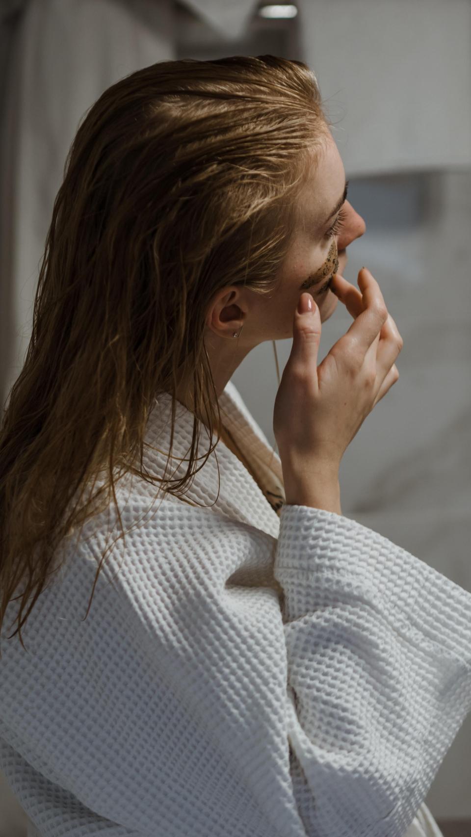 Mujer, con el pelo mojado, aplicándose producto facial.
